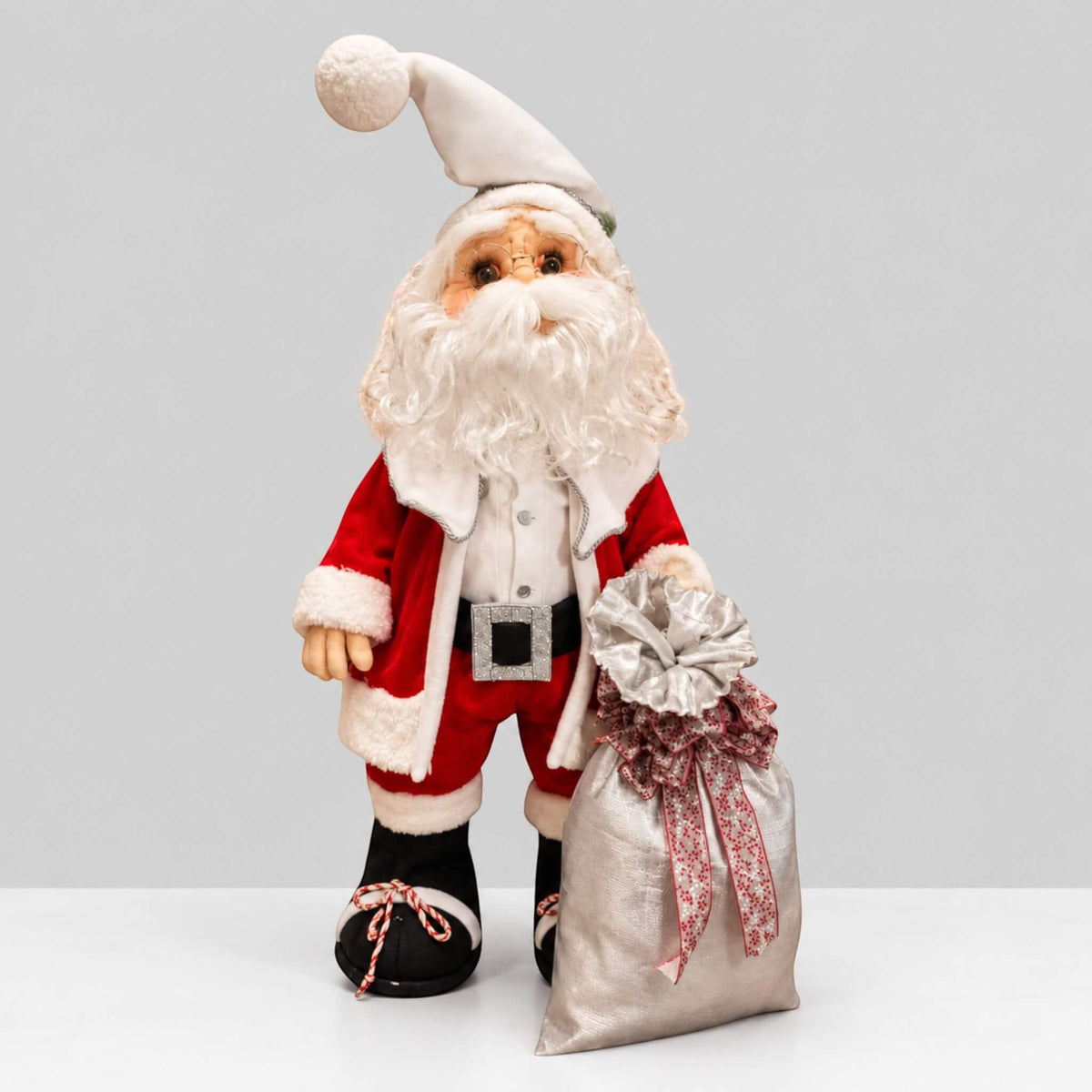 Full-length view of handmade Santa Claus beside a silver gift sack with patterned ribbons.