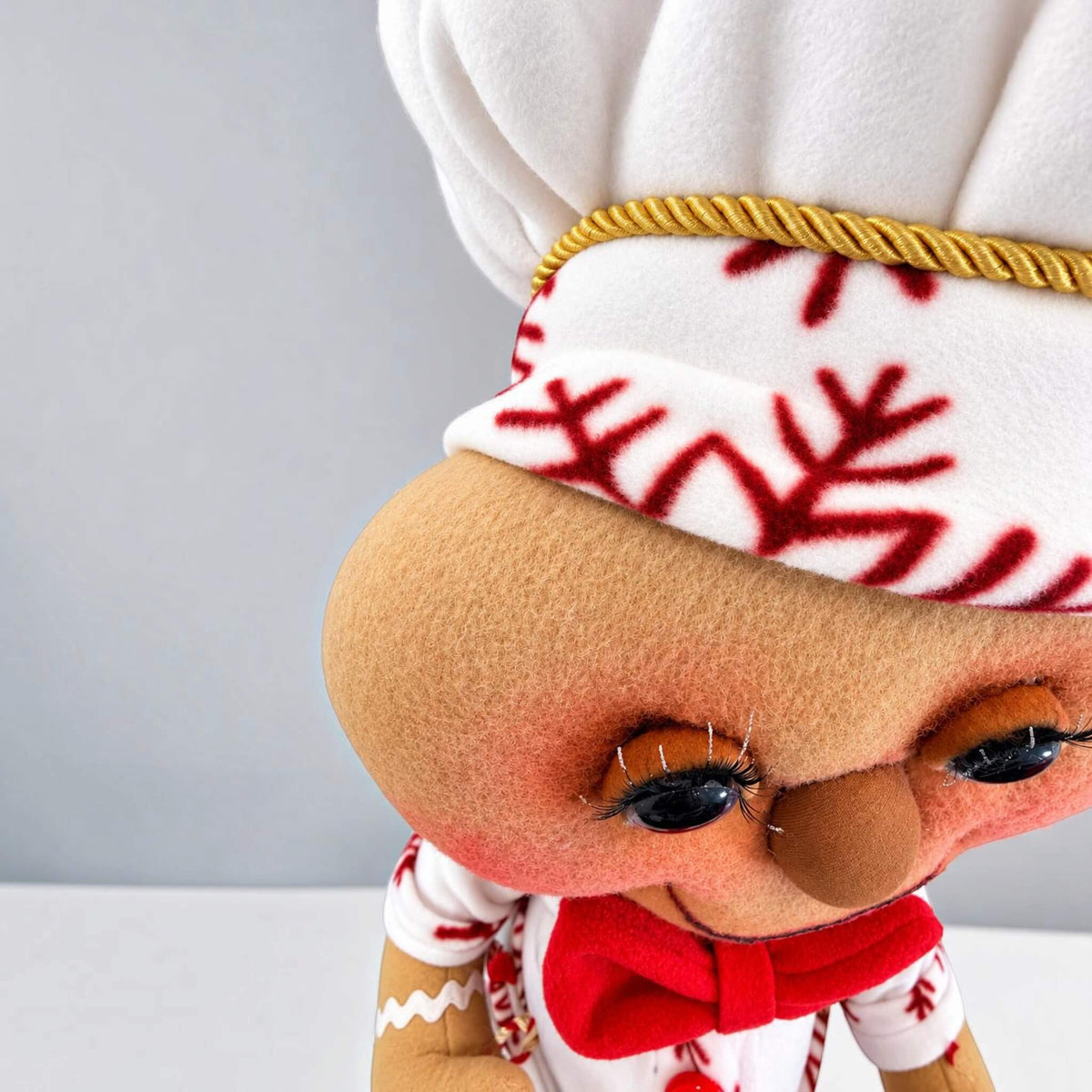 Close-up of handmade Gingerbread Baker face and Christmas chef hat showing detailed fabric texture, eyes, and handcrafted features.