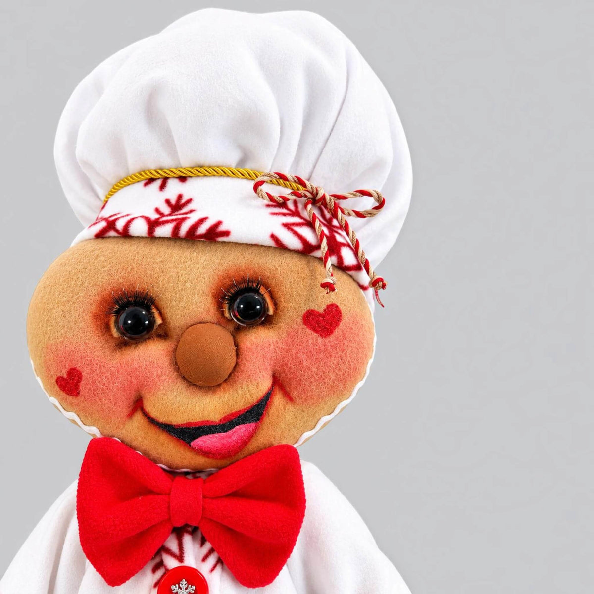 Close-up portrait of handmade Christmas Gingerbread Baker with chef hat, red bow tie, heart cheeks, and detailed handcrafted face