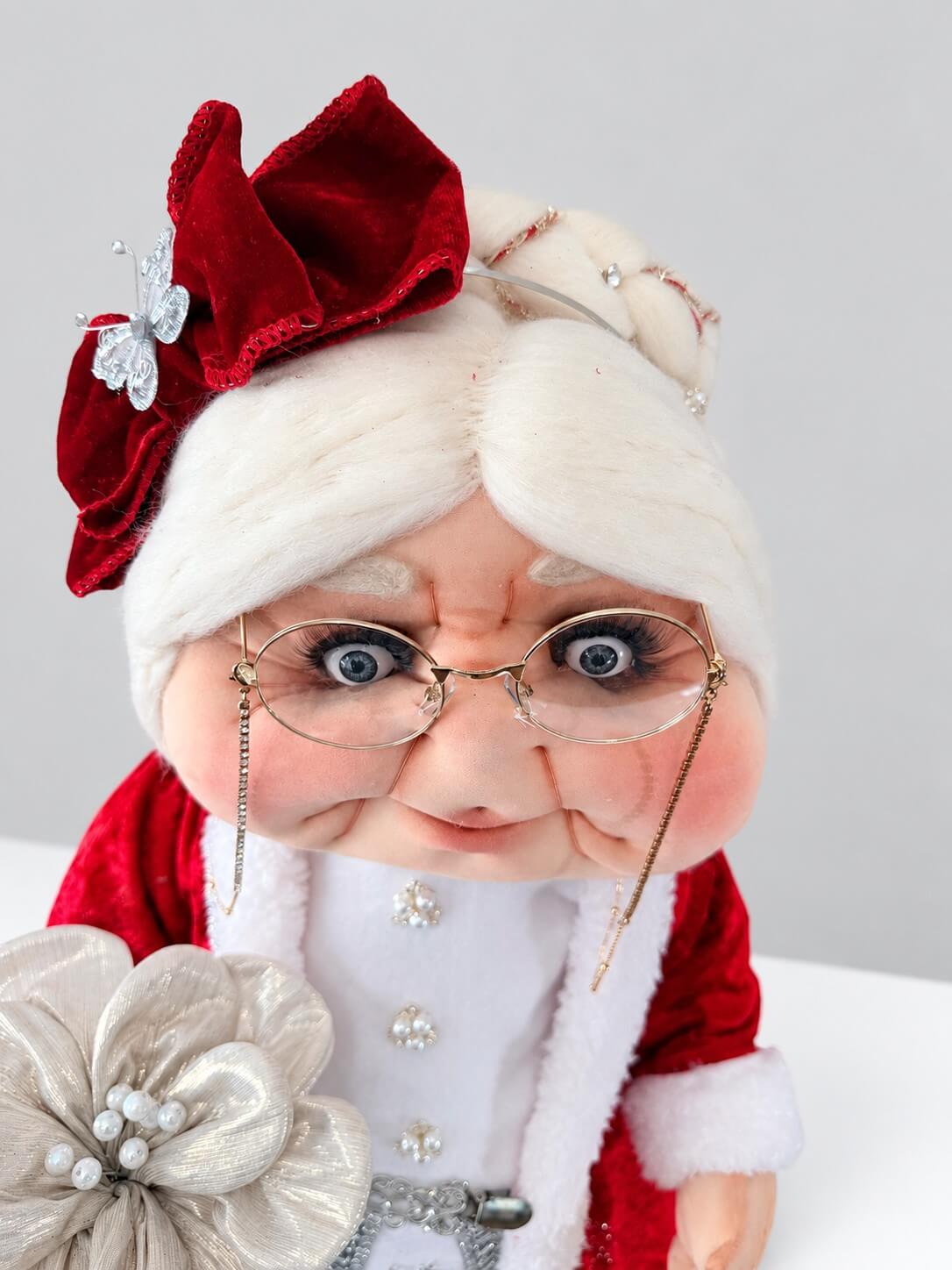 Angled close-up of Mrs. Claus showing her glasses, handcrafted face, white hair, and red headpiece.