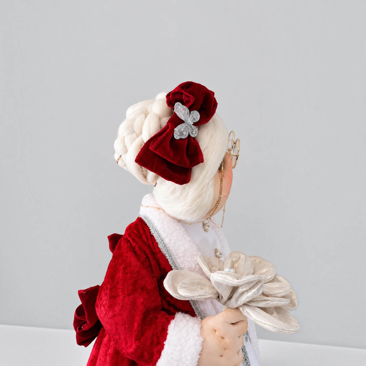 Close-up side view of Mrs. Claus showing her white hairstyle, red bow, glasses, and silver flower.