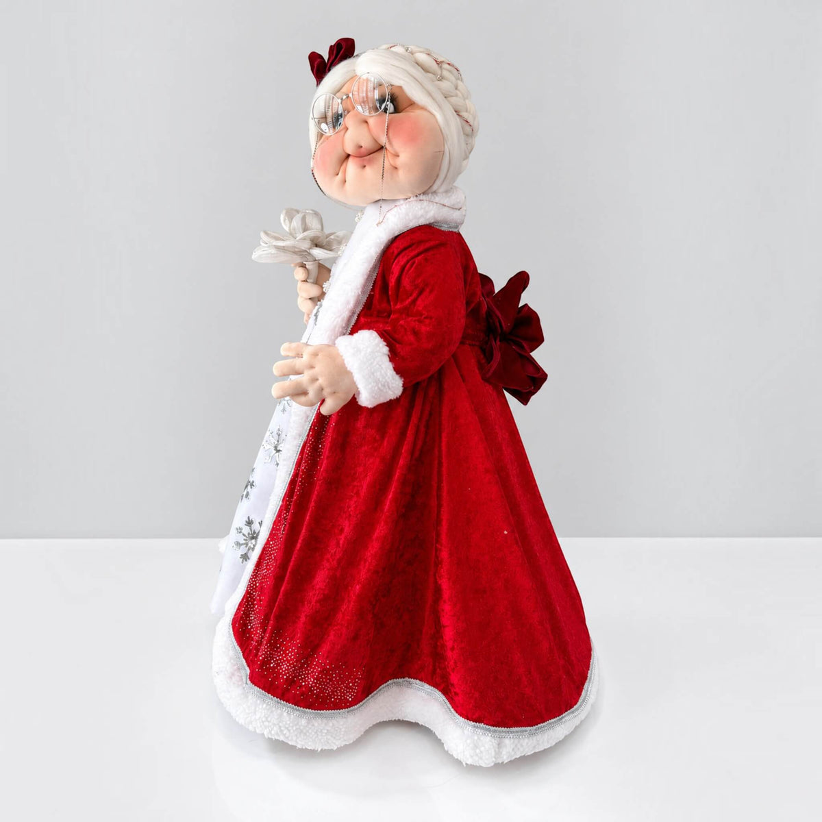 Three-quarter side view of Mrs. Claus holding a silver flower in her red Christmas dress.