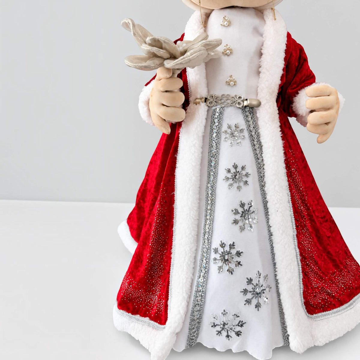 Close-up of Mrs. Claus’s dress showing silver snowflakes, a decorative belt, white trim, and her hands.