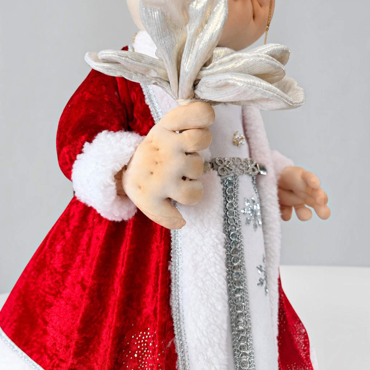Close-up of Mrs. Claus holding a silver flower, with white trim and silver details on her red dress.