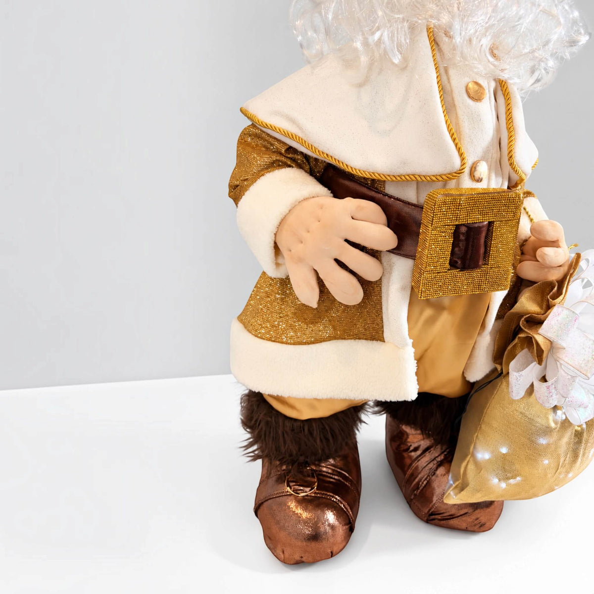 Close-up of Santa Claus’s gold and cream coat, belt, articulated hands, brown boots, and gift bag.