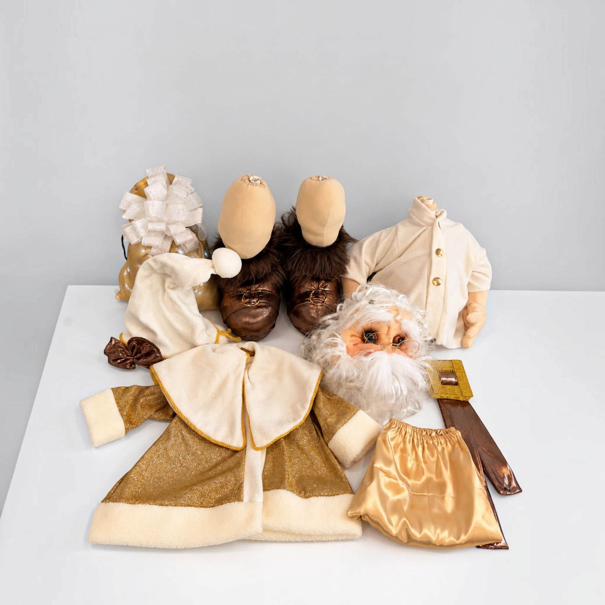 Gold Santa Claus’s removable parts, clothing, boots, belt, and gift bag arranged on a white table.