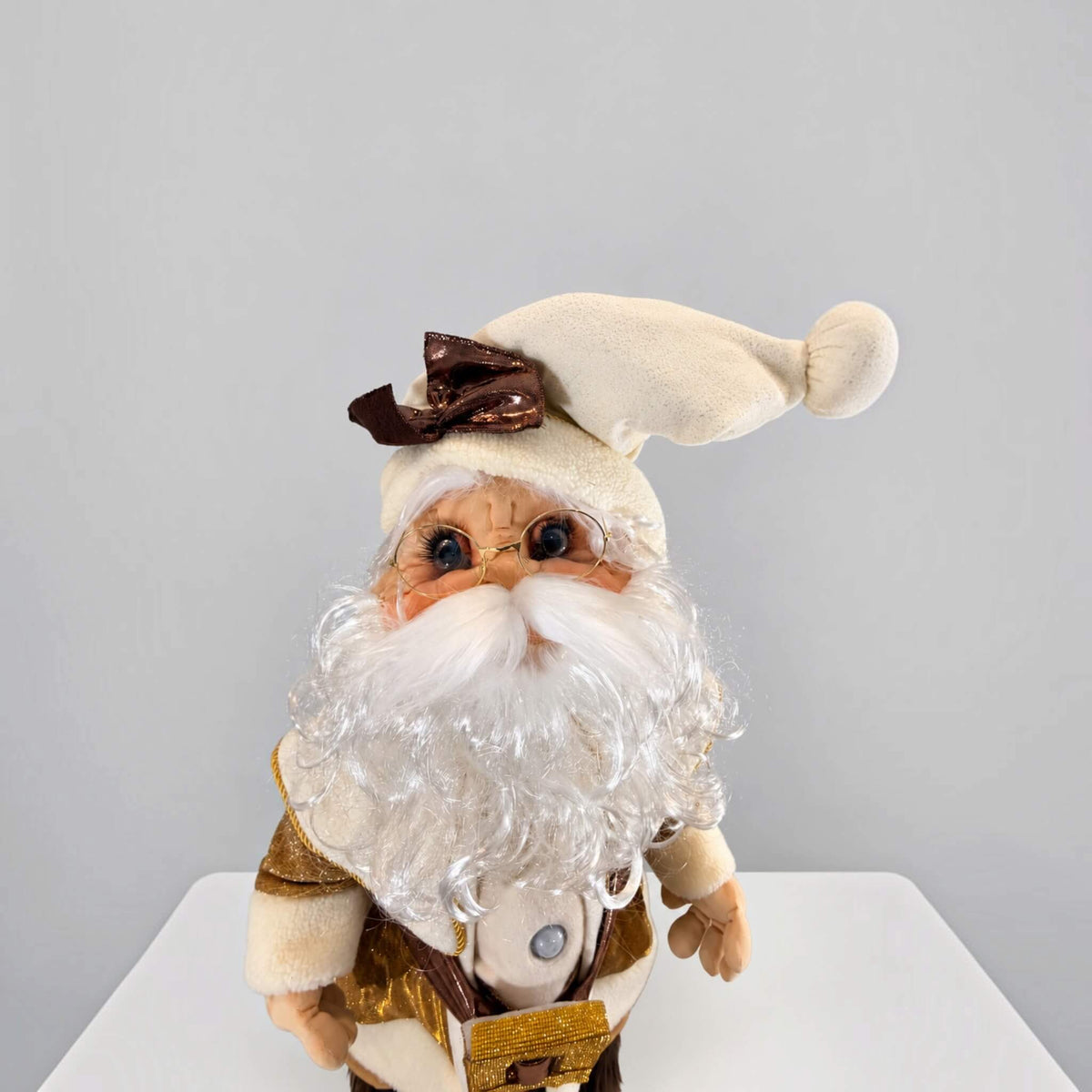 Close-up from above of a handmade Gold Santa Claus showing his detailed face, round glasses, fluffy white beard, cream-colored Christmas hat, articulated hands, and visible motion sensor on his chest.
