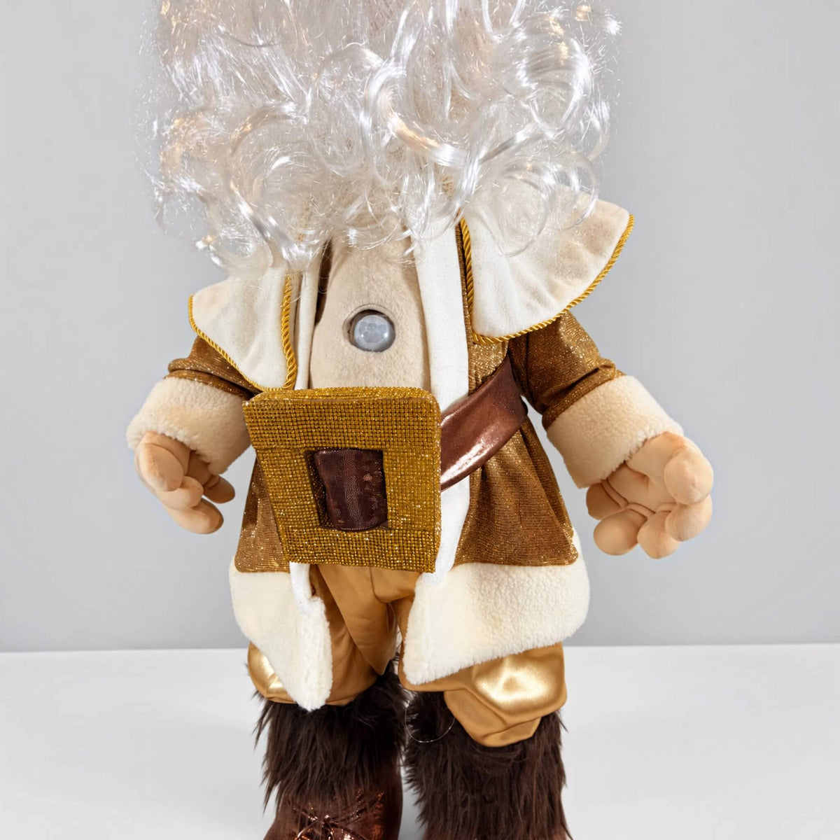 Close-up of a handmade Gold Santa Claus showing the built-in PIR motion sensor on his cream-colored shirt, surrounded by gold-trimmed fabric, a decorative gold pouch, and articulated fabric hands.