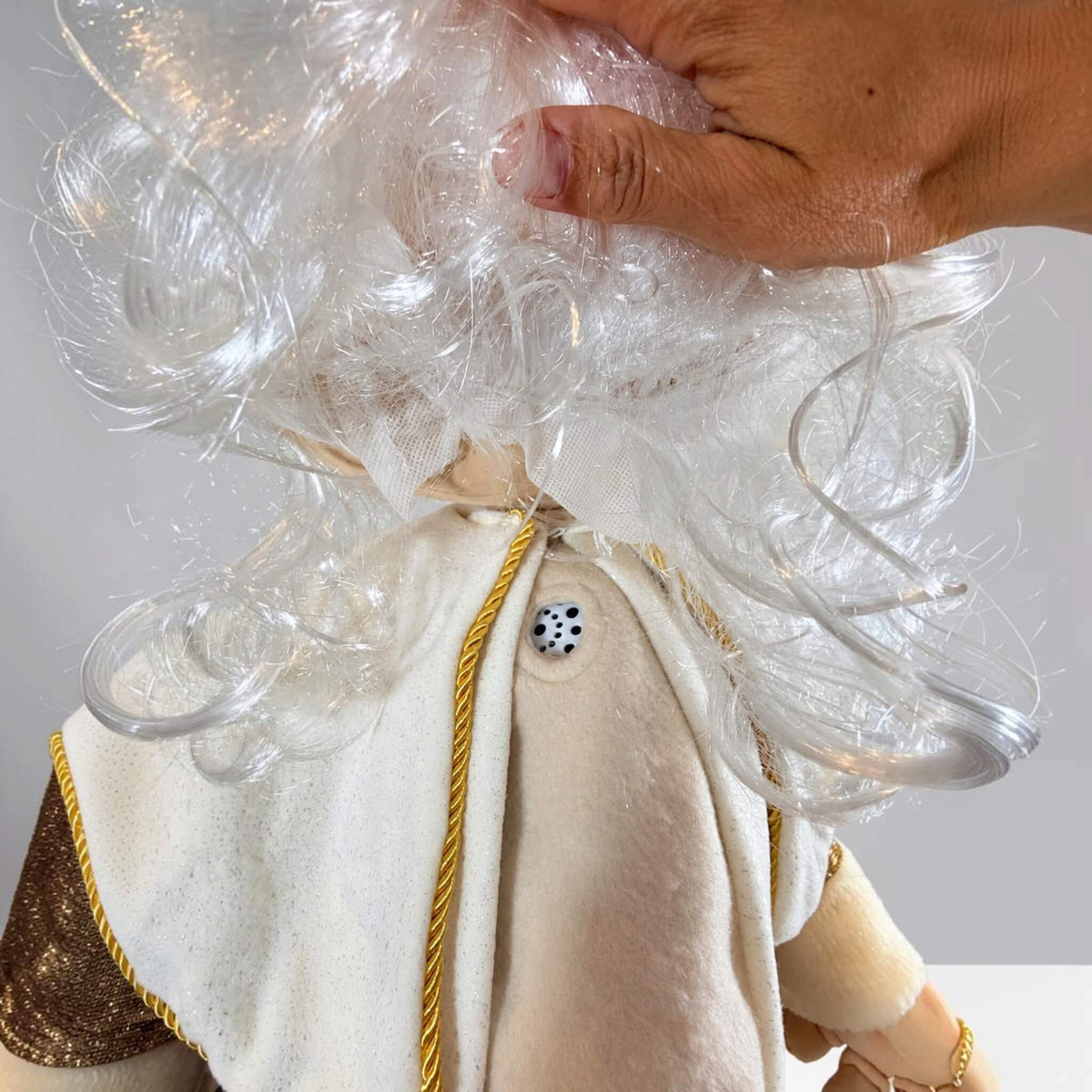 Close-up of the built-in speaker on a handmade Gold Santa Claus Christmas decoration, revealed beneath his white curly beard and positioned on his cream-colored shirt for personalized voice messages and Christmas music.
